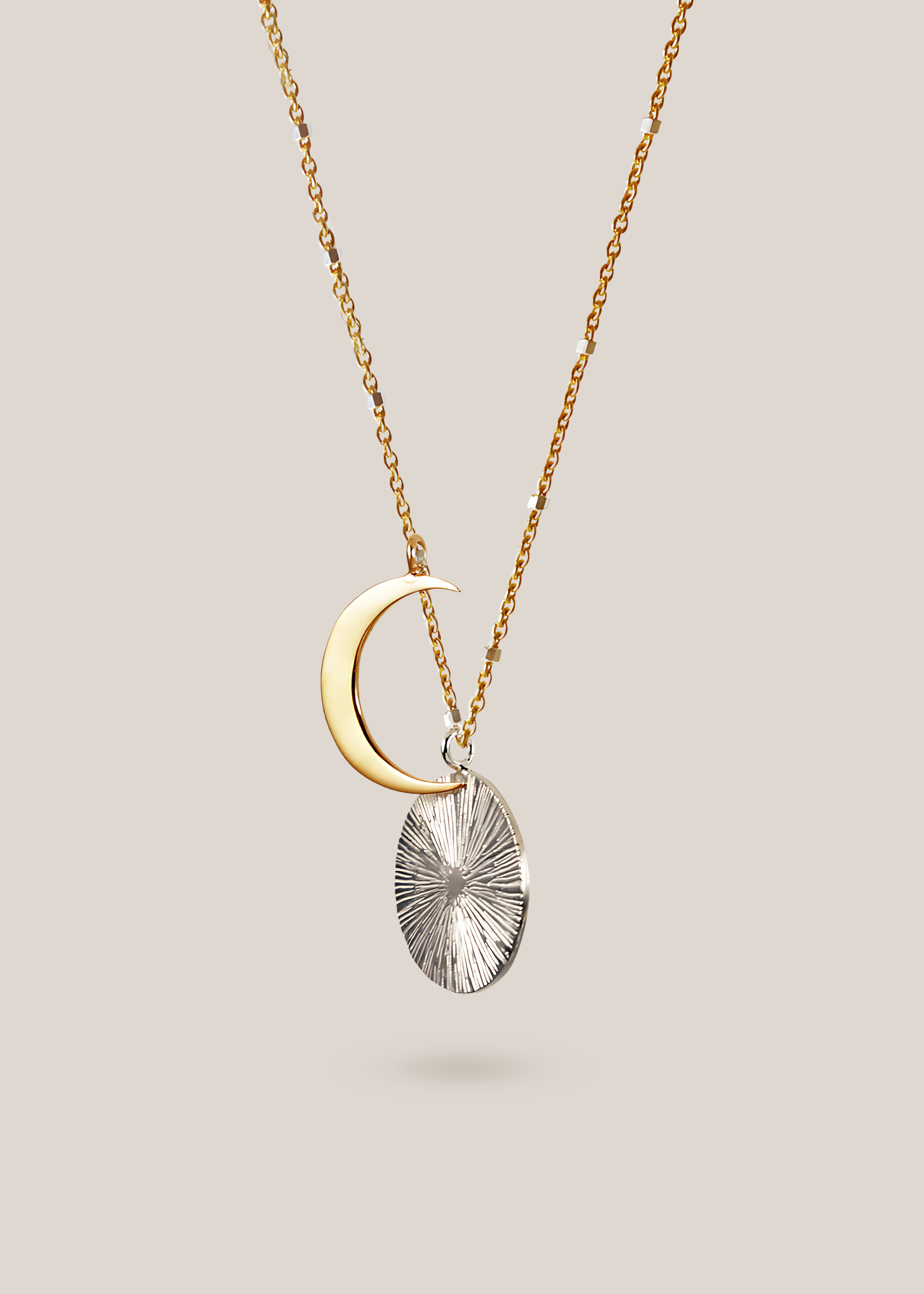 Gold crescent moon and silver textured pendant necklace on a light gray background