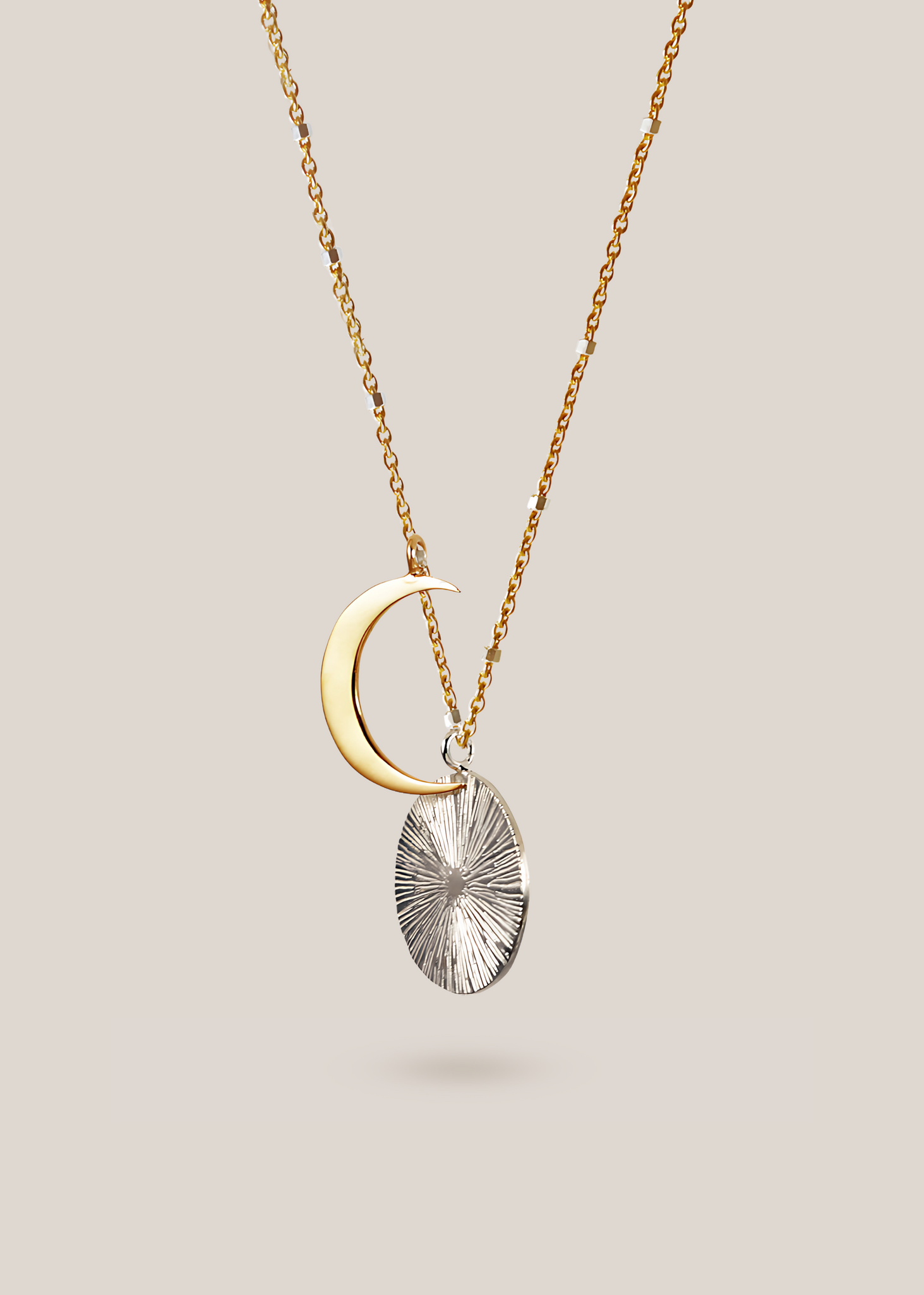 Gold crescent moon and silver textured pendant necklace on a light gray background